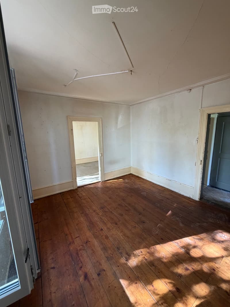 Empty room with wooden flooring, white walls, and two doors, one leading to another room.