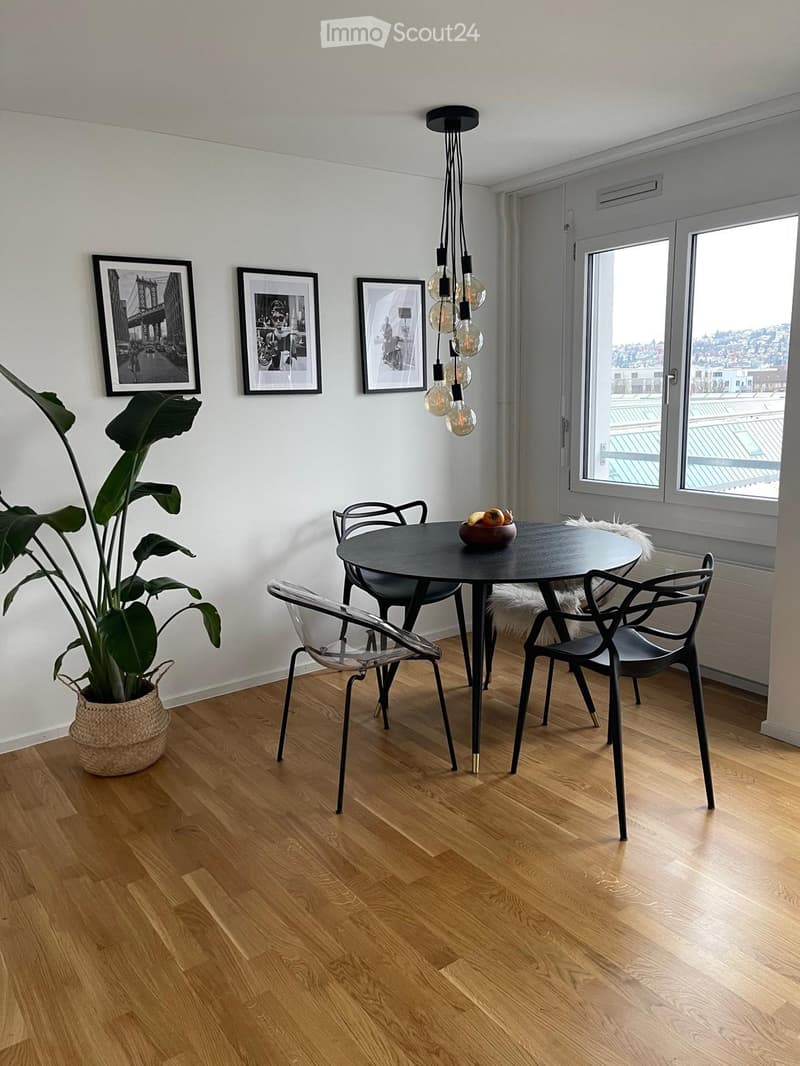 Dining area with a round black table, four chairs, a large leafy plant in a woven basket, and three picture frames on the wall.
