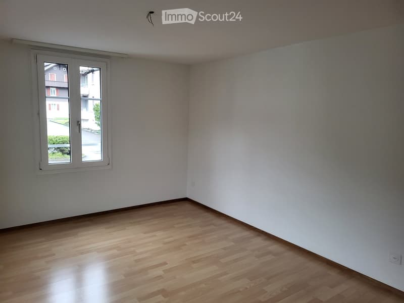 Empty room with wooden flooring and white walls, featuring a single window with a view of the outside.