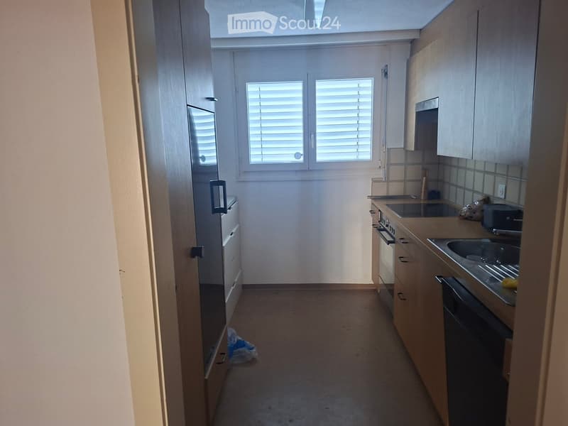 Empty kitchen with light wooden cabinets, a sink, oven, microwave, and a window with blinds.