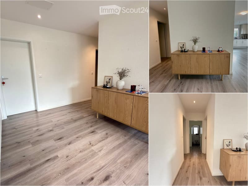 A modern hallway with light wooden flooring, white walls, and a small wooden console table with decorative items on it. The hallway leads to a bathroom and other rooms.
