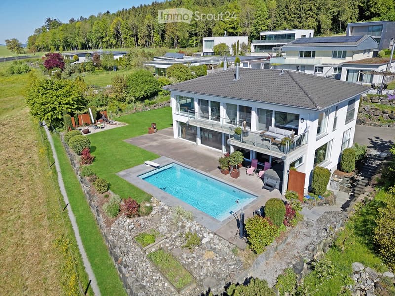 Aerial view of a modern two-story house with a large balcony, swimming pool, and well-maintained garden.