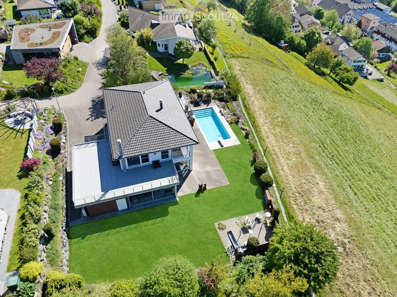 Aerial view of a suburban house with a well-maintained lawn, a swimming pool, and surrounding greenery.
