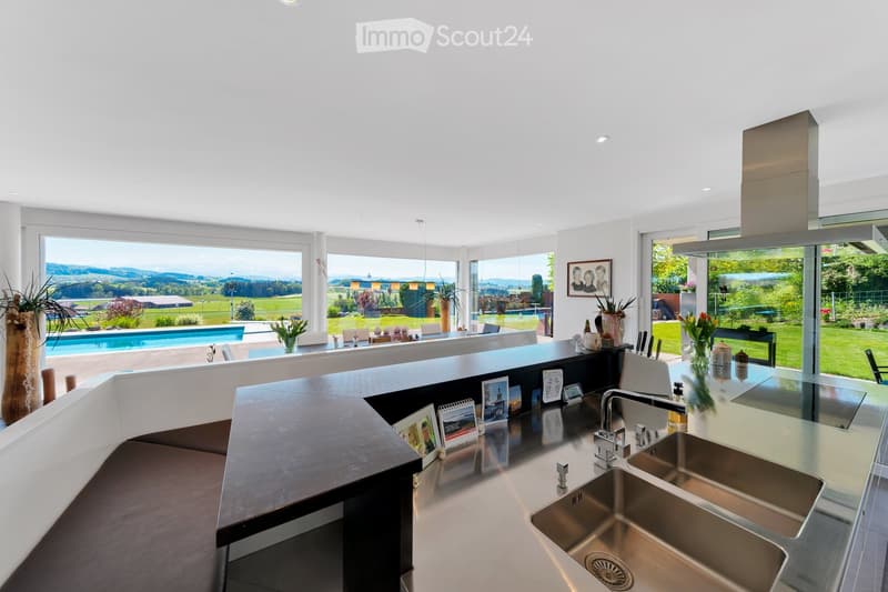 Modern kitchen with stainless steel sink, large windows offering a scenic view, and decorative items on the counter.