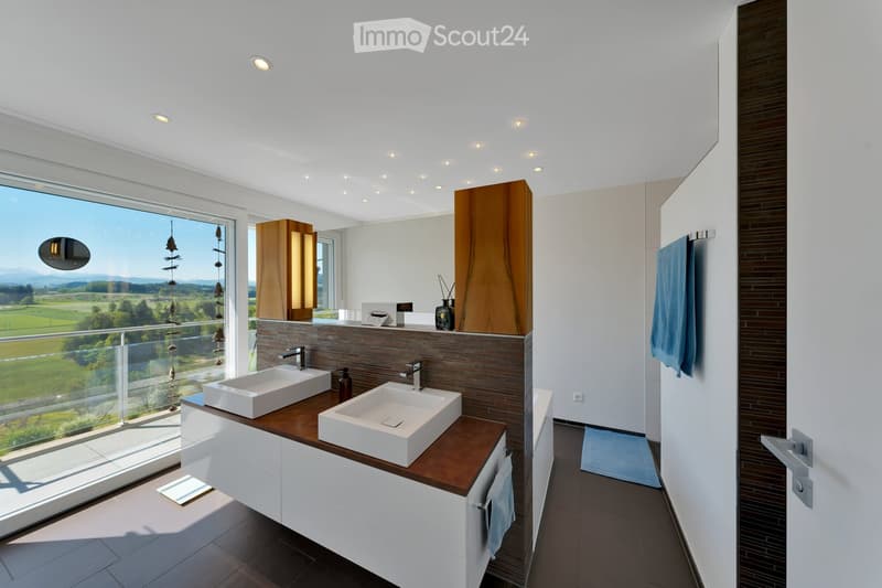 Modern bathroom with double sinks, wooden countertop, large window offering scenic view, and contemporary fixtures.