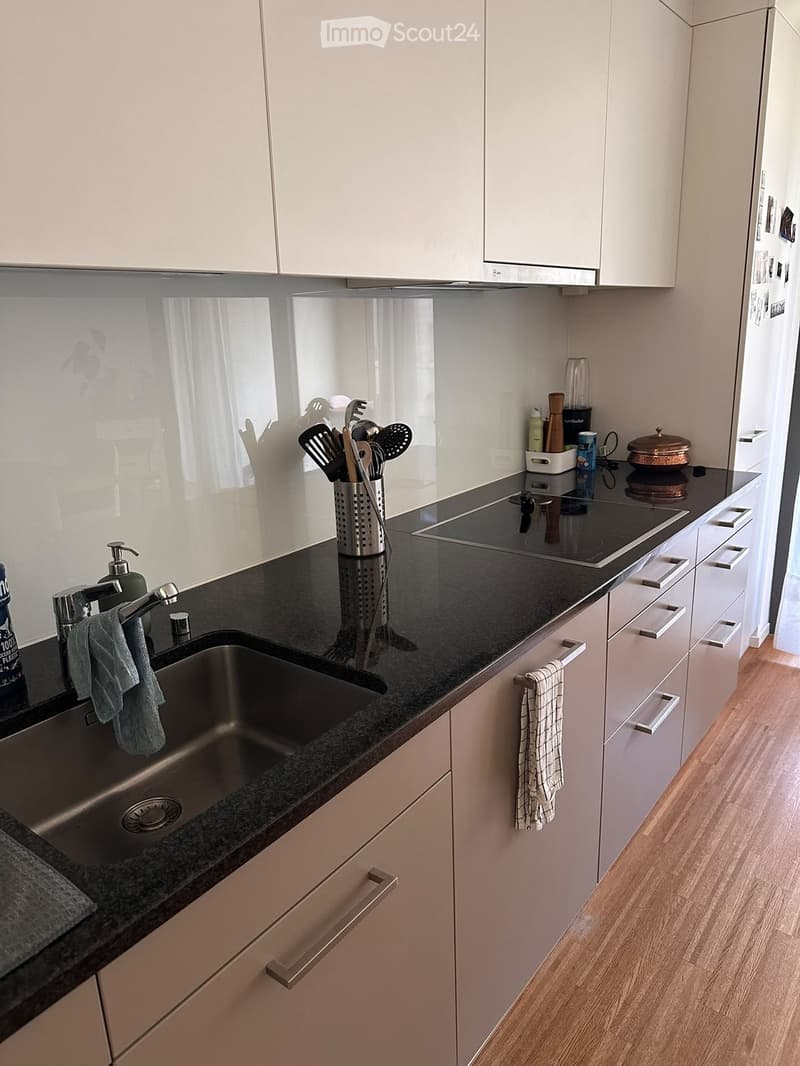 Modern kitchen with white cabinets, black granite countertop, stainless steel sink, electric stove, and various kitchen utensils.