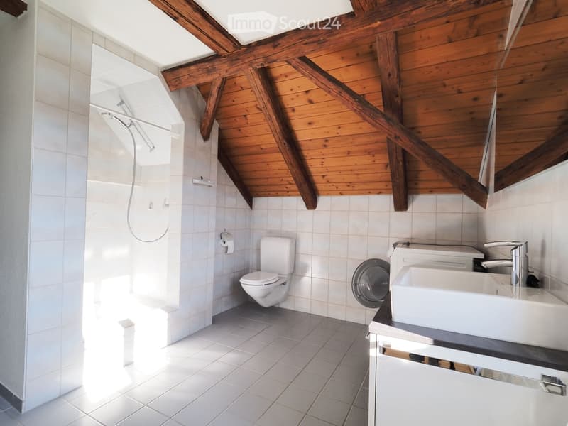 Modern bathroom with white tiles, wooden slanted ceiling beams, a toilet, a sink with a faucet, a shower, and a mirror.