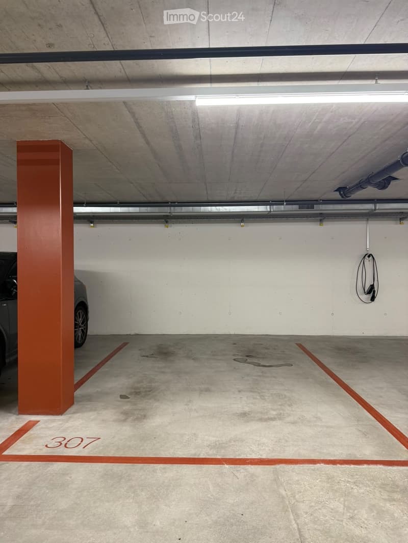 Underground parking space with concrete floors and walls, marked parking spots, and a single car partially visible.