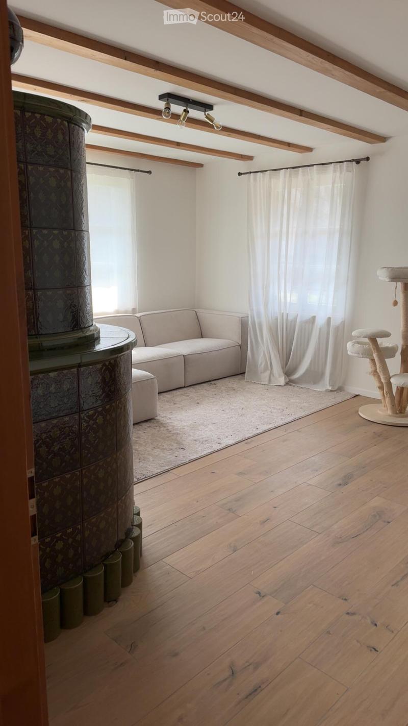 Bright living room with wooden floors, exposed wooden beams, a modern sofa, a cat tree, and a round table with a decorative column.