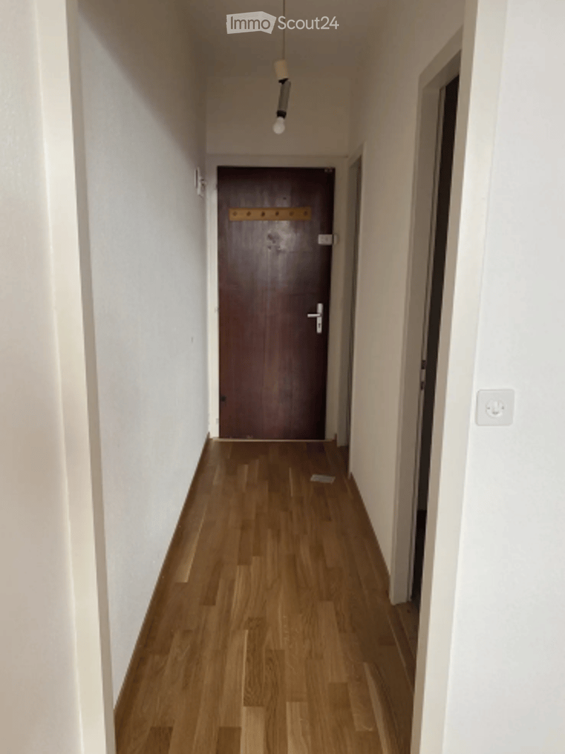 Empty hallway with wooden flooring, white walls, and a closed wooden door at the end.