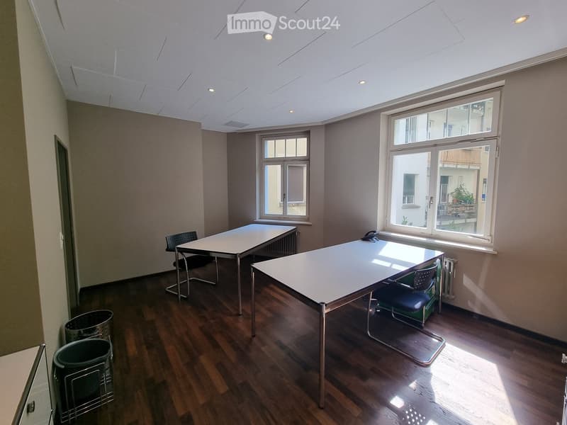 Bright room with wooden flooring, two tables, chairs, and trash bins near the wall.