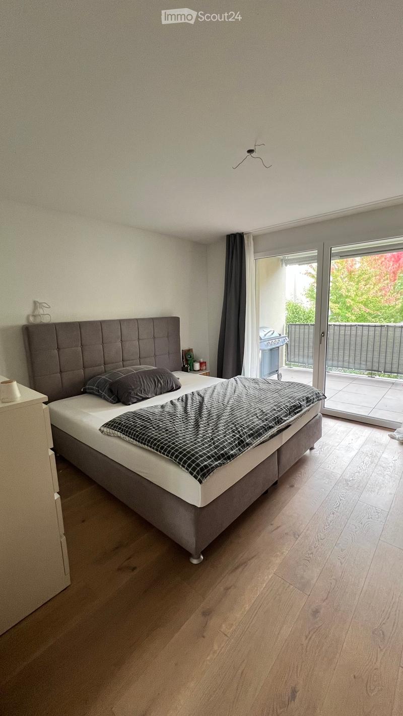 Modern bedroom with a large bed, nightstand, and sliding glass door leading to a balcony.