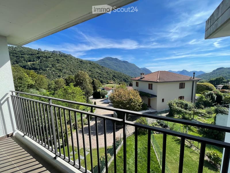 Balcony overlooking a scenic valley with a house, trees, and mountains in the background.