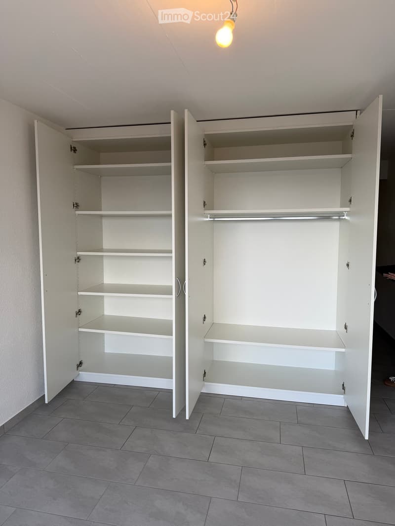 Empty room with white built-in cabinets and shelves, grey tiled floor, and a hanging light fixture.