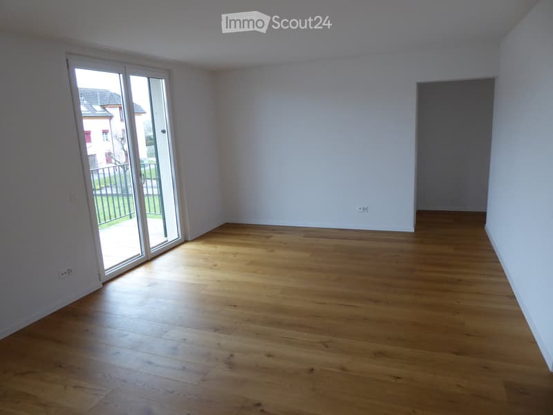 Empty room with light wooden flooring, white walls, and a large sliding glass door leading to a balcony or outdoor area.
