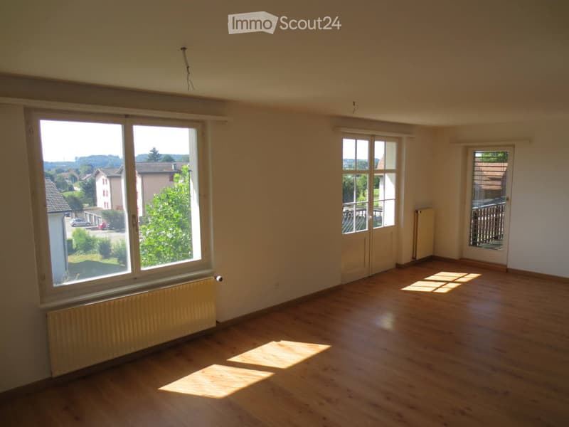 Empty room with wooden flooring, large windows, and radiators. No furniture or equipment present.