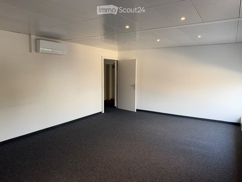 Empty room with white walls, carpeted floor, and a mounted air conditioning unit. Two open doors lead to adjacent spaces.