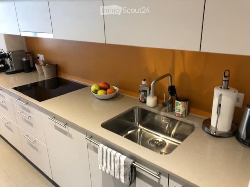Modern kitchen with white cabinets, a stainless steel sink, and a countertop with a bowl of fruit, a coffee maker, and other small items.