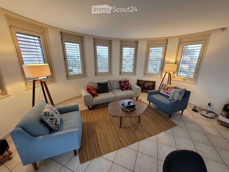 Modern living room with large windows, grey sofa, coffee table, floor lamp, and decorative pillows.