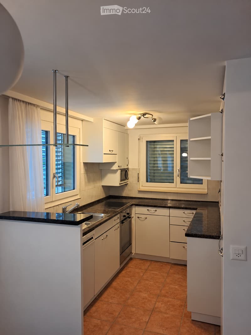 Modern kitchen with white cabinets, black countertops, stainless steel appliances, and a central island with a sink and faucet.