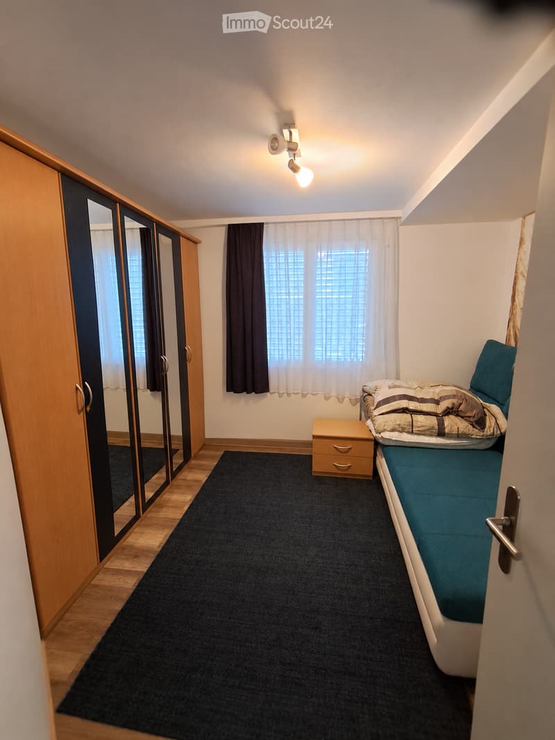 Cozy bedroom with a single bed, nightstand, wardrobe with mirrored doors, and a window with curtains.