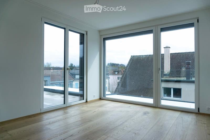 Bright, empty room with large glass sliding doors leading to a terrace, wooden flooring, and white walls.