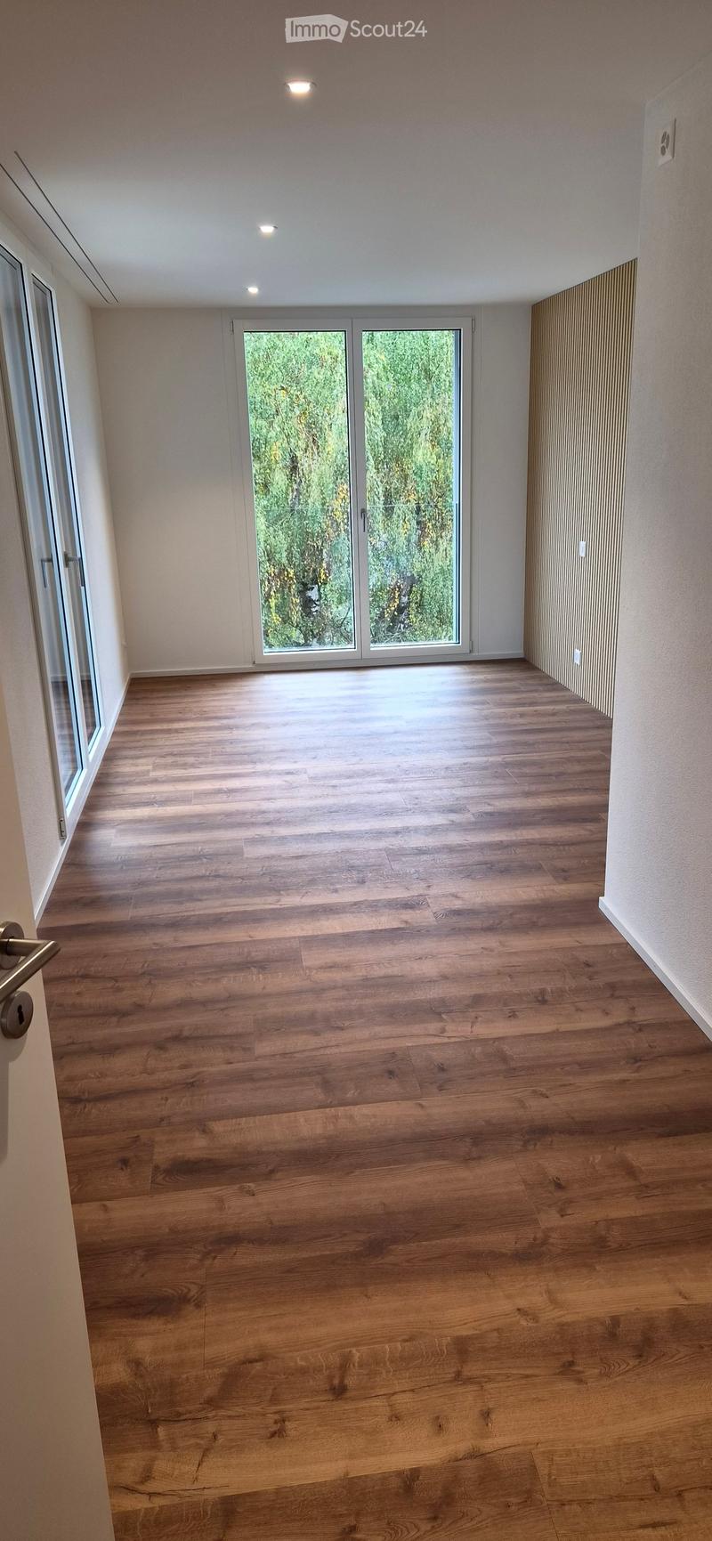 Empty room with wooden flooring, large sliding glass doors, and white walls.
