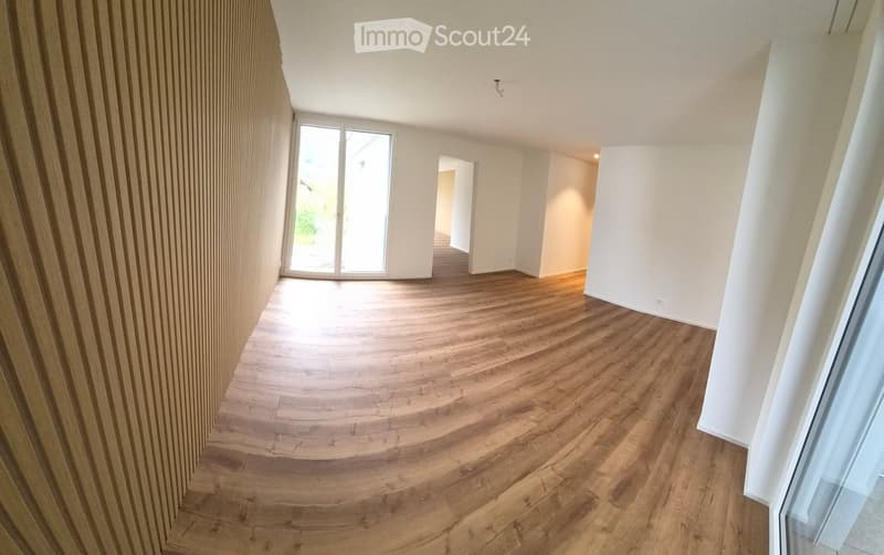 Empty room with wooden flooring, white walls, and large windows allowing natural light to enter. The space is clean and unfurnished, with no visible furniture or decorations.