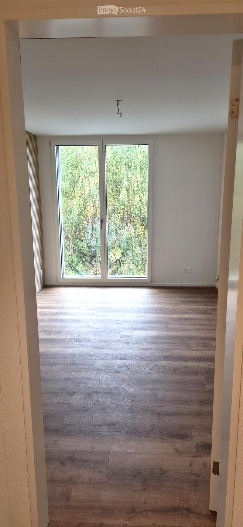 Empty room with wooden flooring, large sliding glass doors leading to an outdoor area, white walls, and a visible electrical outlet.