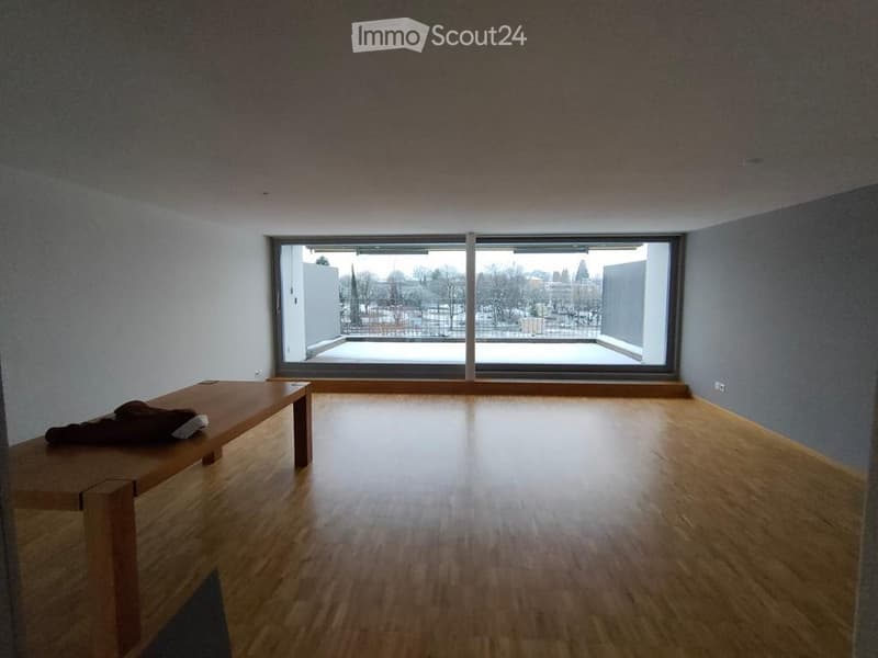 Empty room with wooden flooring, large window, and a small wooden table with a jacket on it.