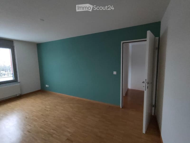 Empty room with wooden flooring, green accent wall, and an open doorway leading to another room.