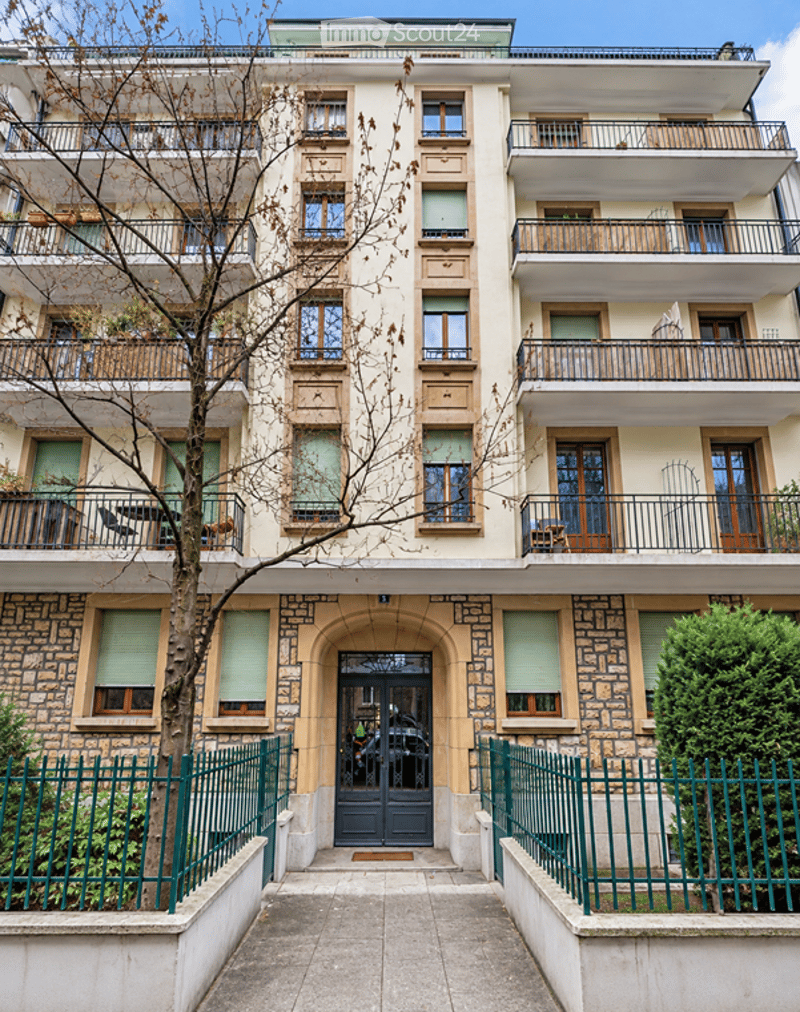 Multi-story residential building with balconies, stone facade, and green metal fence.