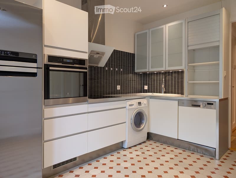Modern kitchen with white cabinets, stainless steel appliances, and a geometric tile floor.