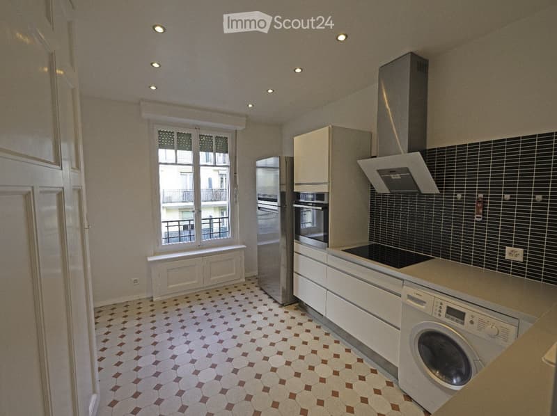 Modern kitchen with white cabinets, stainless steel appliances, and a tiled floor. Features a refrigerator, oven, dishwasher, washing machine, and a range hood.