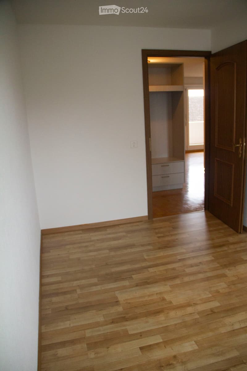 Empty room with wooden flooring and white walls, featuring an open closet with shelves and drawers visible in the background.