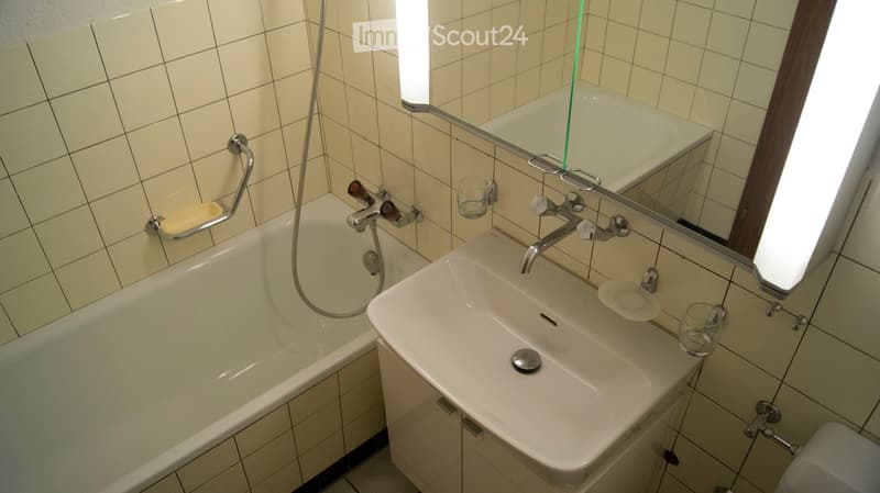 Bathroom with a bathtub, sink, mirror, and cup on the sink counter.