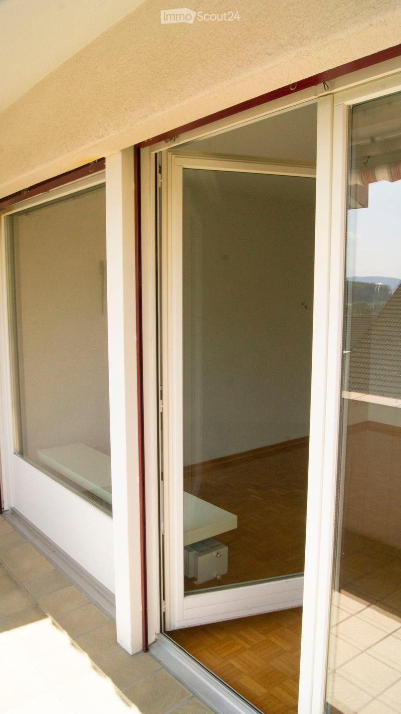 Open sliding glass doors leading to a balcony with wooden flooring and a view of the surrounding area.