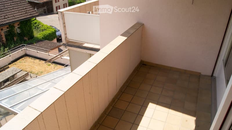 Balcony with tiled floor, beige walls, metal railing, and a view of a neighboring building and greenery.
