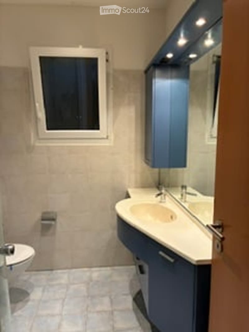 Modern bathroom with a white tiled floor, a blue cabinet, a sink with a mirror, and a toilet.