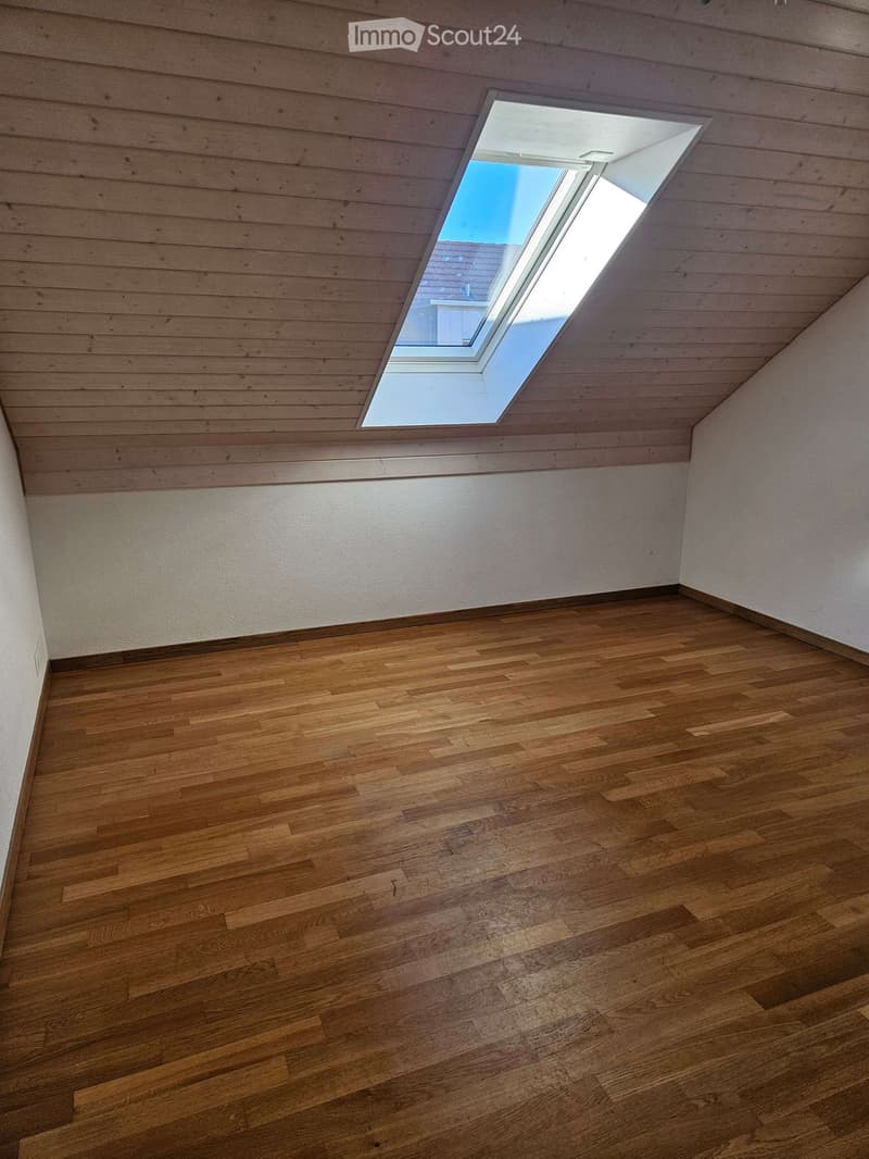 Empty room with wooden flooring and white walls, featuring a skylight window in the ceiling.