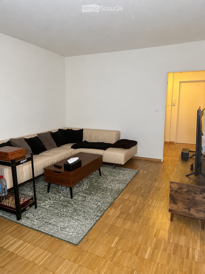 Living room with a light-colored sectional sofa, wooden coffee table, side table, and a television in the adjacent room.