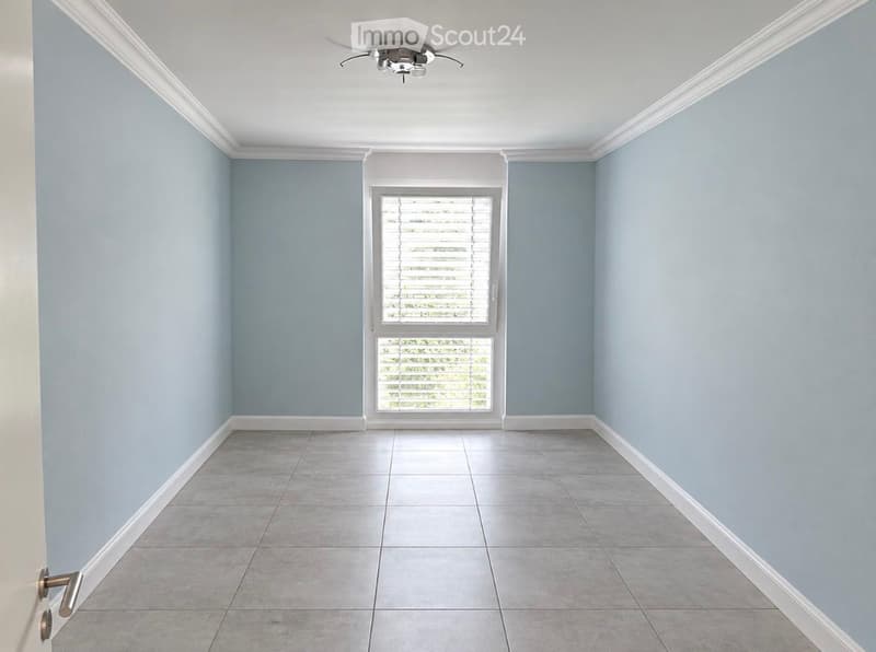 Empty room with light blue walls, tiled floor, and a single window with blinds. No furniture or equipment present.