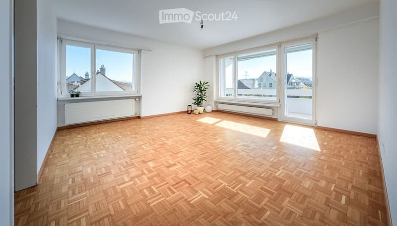 Empty room with wooden herringbone flooring, large windows, radiators, and a small plant in the corner.