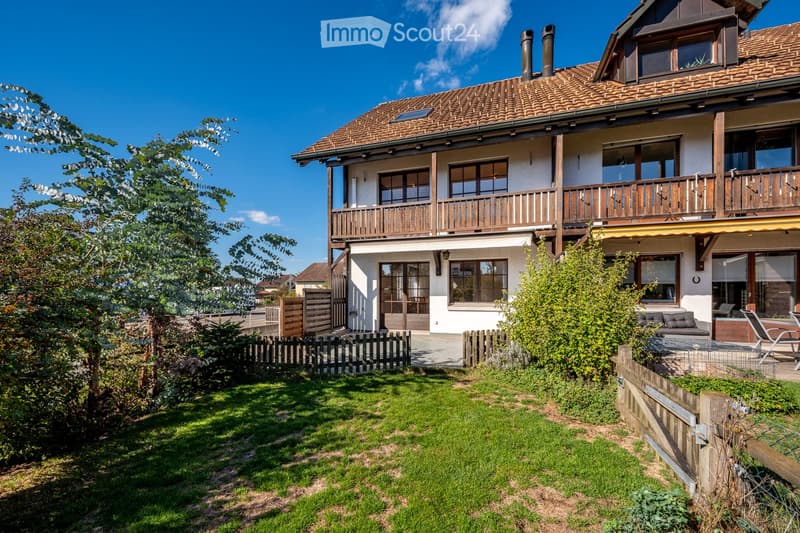 Two-story house with a tiled roof, wooden balcony, and well-maintained garden with a lawn and wooden fence.