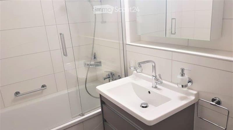 Modern bathroom with white tiles, a sink with a chrome faucet, a mirror cabinet, and a shower area with a glass enclosure.