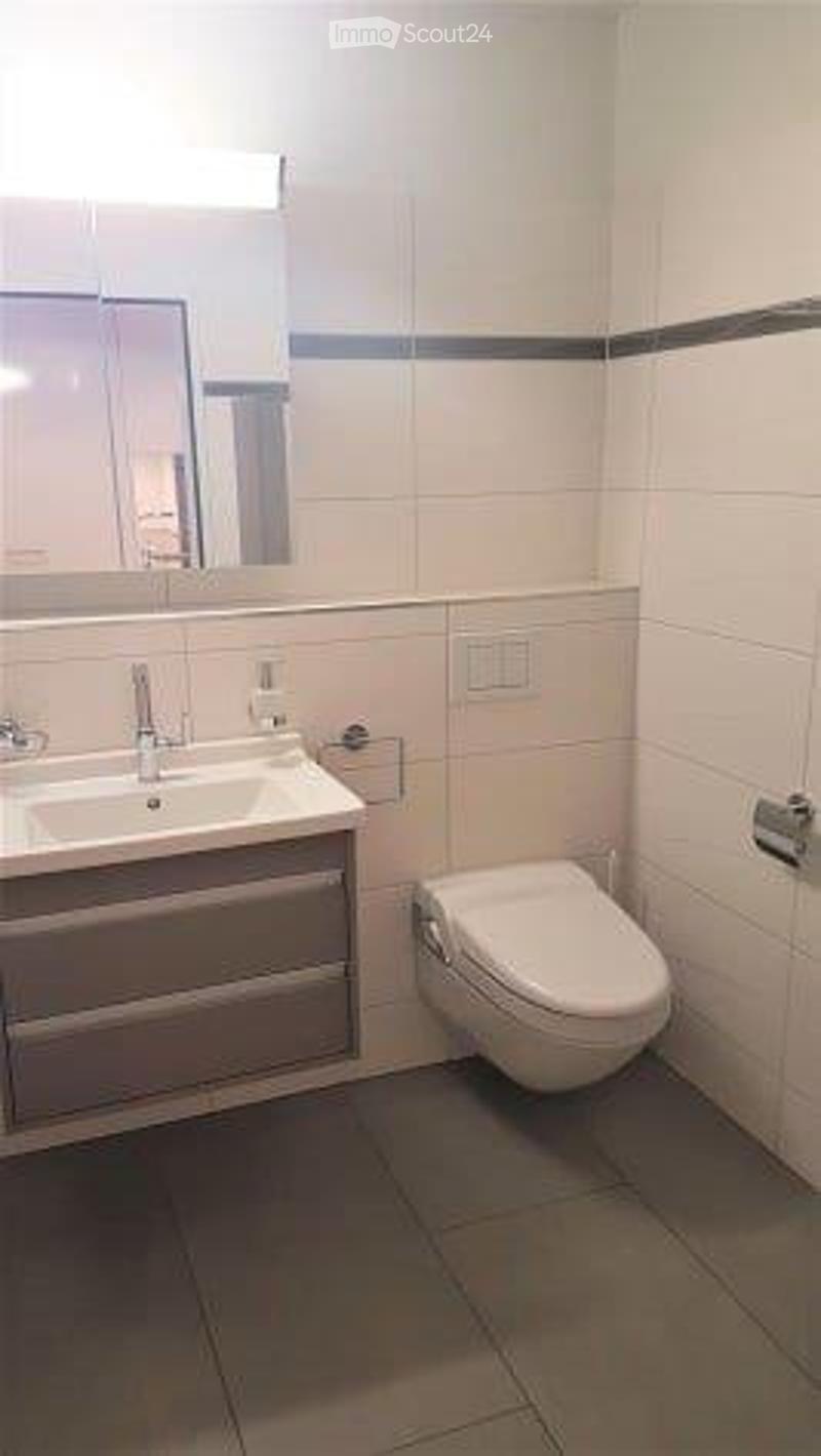 Modern bathroom with a white sink, mirror, and toilet. The walls are tiled in light beige with a dark accent stripe near the top.