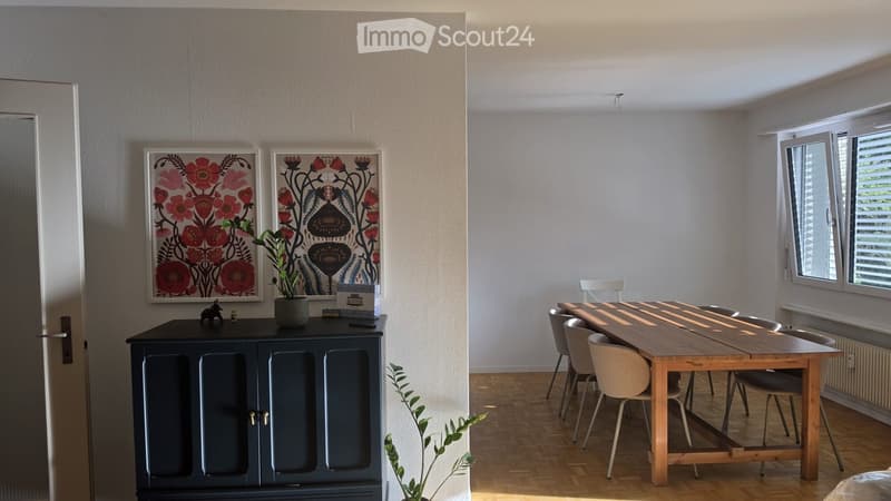 Bright dining area with a wooden table, chairs, a dark blue cabinet, and two framed floral pictures on the wall.