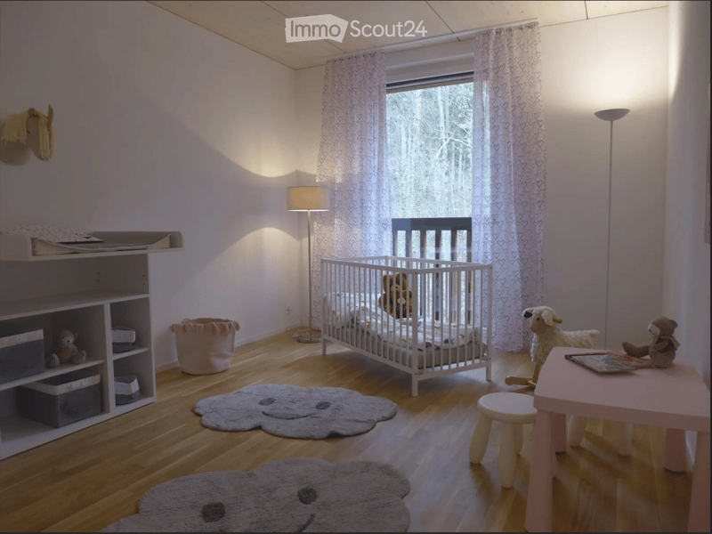Brightly lit children's bedroom with wooden flooring, a crib, a small table with a stool, shelves, and toys.