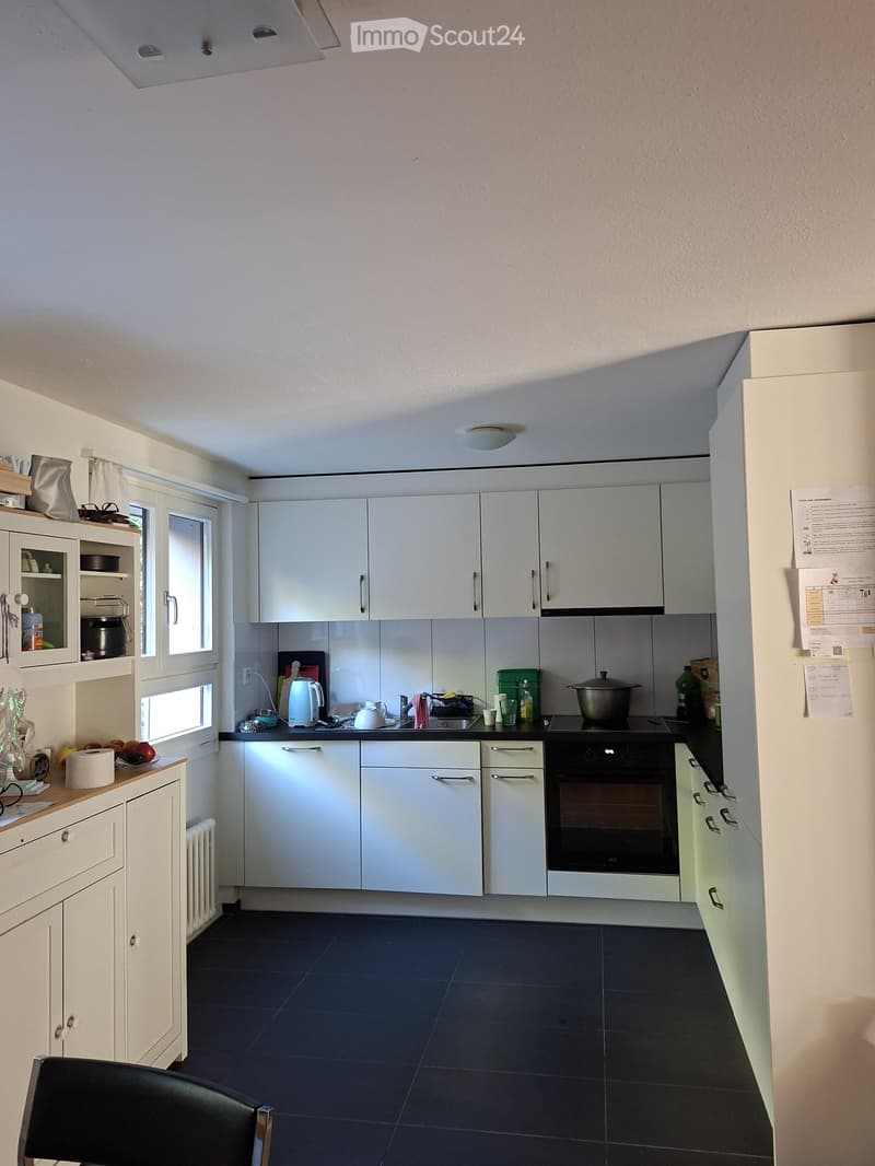 Modern kitchen with white cabinets, black countertops, and stainless steel appliances. Includes a refrigerator, oven, sink, and various kitchen items on the counter.