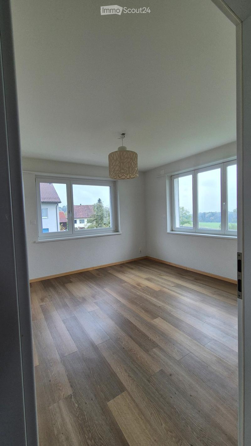 Empty room with wooden flooring, white walls, large windows, and a hanging light fixture.